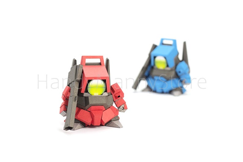 Pu&ograve; includere: Due figurine di robot, una rossa e una blu, sono esposte su sfondo bianco. Il robot rosso &egrave; in primo piano, con una pistola attaccata. Ogni robot ha un globo giallo brillante al centro.