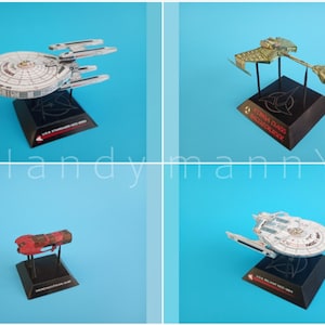 May include: Four model starships on black stands against a blue background. The models include a white and gray ship with a saucer section, a gold ship, a red ship, and another white and gray ship. Each stand has text.