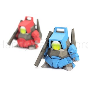 Pu&ograve; includere: Due figure simili a robot, una rossa e una blu, sono posizionate su uno sfondo bianco. Ogni figura ha un grande occhio rotondo giallo-verde e un accessorio a forma di pistola. Le figure sono fatte di forme geometriche angolari.