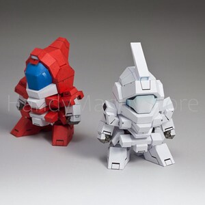 May include: Two stylized robot figures. One is red with blue and white accents, the other is white. Both have blocky designs and are posed in a squatting position. The robots appear to be toys or models.