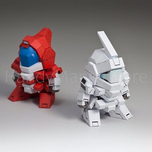 May include: Two stylized robot figures. One is red with white and blue accents, the other is white. Both have blocky designs and are posed in a crouching position. The background is a solid gray.