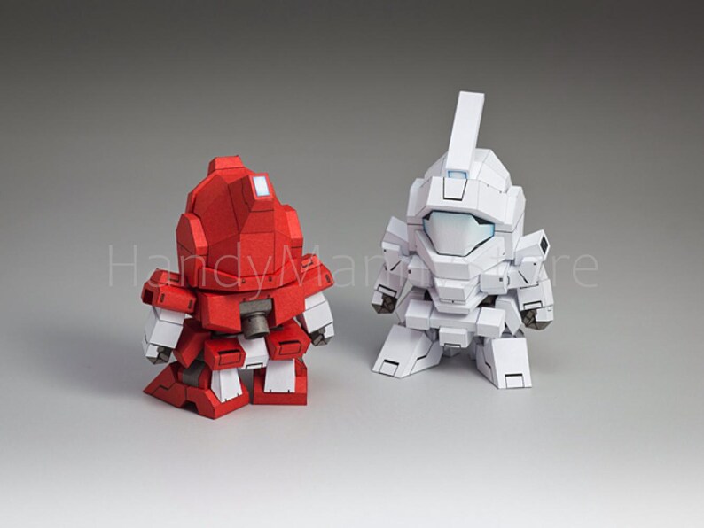 May include: Two stylized robot figures, one red and one white, stand side-by-side. The red robot has white accents, while the white robot has a blue visor. Both figures have a blocky, geometric design, suggesting a toy or collectible item.