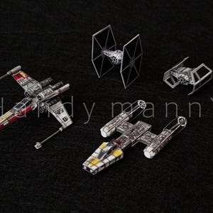 May include: A collection of Star Wars model spacecraft, including an X-wing, Y-wing, and two TIE fighters, are displayed against a dark background. The models are detailed with various colors and designs, and the text "- handy manny -" is visible.