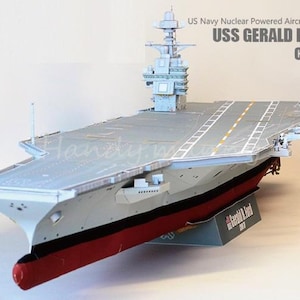 Könnte beinhalten: Ein Modell des Flugzeugträgers USS Gerald R. Ford (CVN-78). Das Modell ist grau, rot und schwarz, mit dem Text "US Navy Nuclear Powered Aircraft Carrier" und dem Schiffsnamen. Es hat ein detailliertes Flugdeck und Aufbauten.