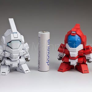 May include: Two robot figurines, one white and one red, stand on a white surface. A standard AA battery is between them. The white robot has a tall, rectangular headpiece. The red robot has a blue visor.