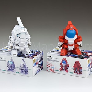 May include: Two robot action figures, one white and one red, sit atop their respective boxes. The white robot has a rectangular head and a long antenna. The red robot has a blue visor. The boxes have illustrations of the robots.
