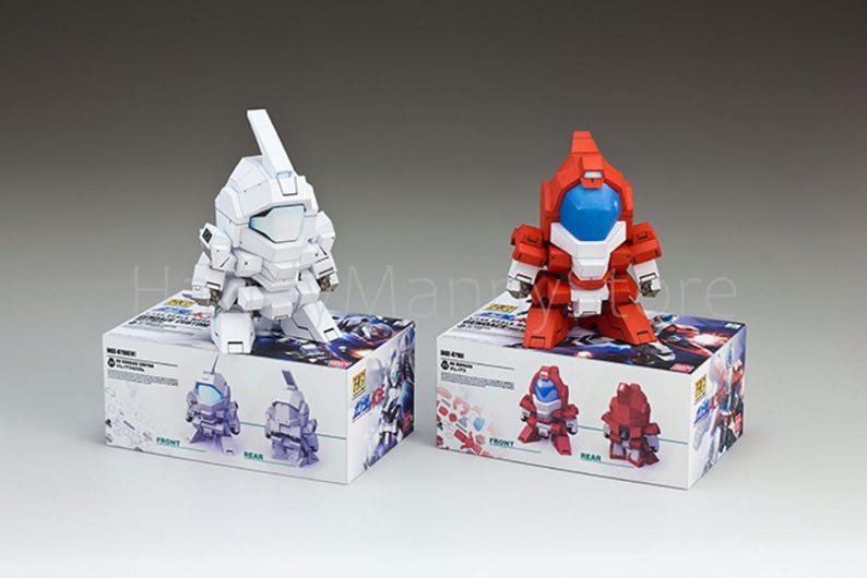 May include: Two robot action figures, one white and one red, sit atop their respective boxes. The white robot has a rectangular head and a long antenna. The red robot has a blue visor. The boxes have illustrations of the robots.