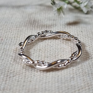May include: A silver ring with a twisted design and small beads.