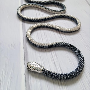 Pode incluir: Um colar de cobra de contas prateadas e pretas com um fecho de cabeça de cobra prateado.