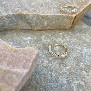 Könnte beinhalten: Zwei goldene Ringe mit einer Reihe von klaren, rechteckigen Steinen. Die Ringe liegen auf einer hellbraunen, strukturierten Oberfläche.