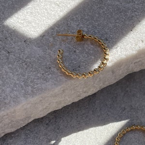 Könnte beinhalten: Goldene Creolen mit Perlenmuster. Die Ohrringe sind klein und zart.