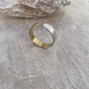 Könnte beinhalten: Ein gold- und silberfarbenes Metall-Armreif-Armband mit einem schlichten, minimalistischen Design.