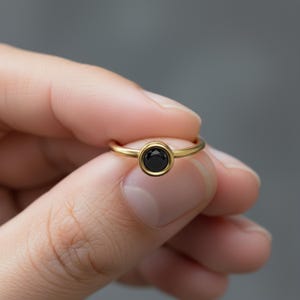 Faceted Onyx Ring: A person's hand holding a gold ring with a black gemstone, specifically a diamond, on the ring finger.