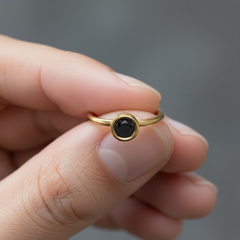 Faceted Onyx Ring: A person's hand holding a gold ring with a black gemstone, specifically a diamond, on the ring finger.