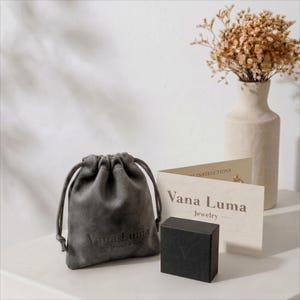 a gray leather pouch, a small black box, and a card with text, all placed on a white surface.