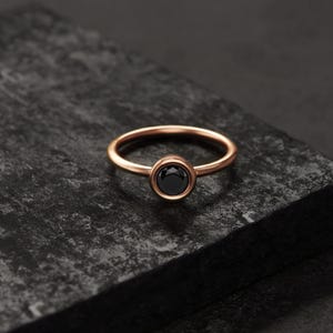A simple gold ring with a black gemstone sits on a dark surface.