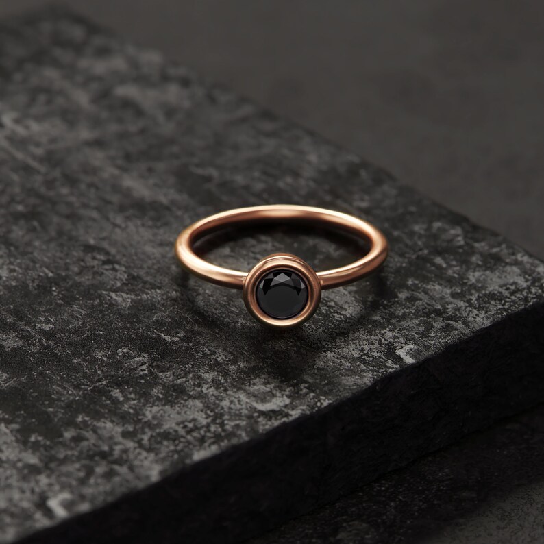 A simple gold ring with a black gemstone sits on a dark surface.