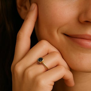A close-up of a person's hand wearing a gold ring with a blue gemstone, resting on the person's chin.