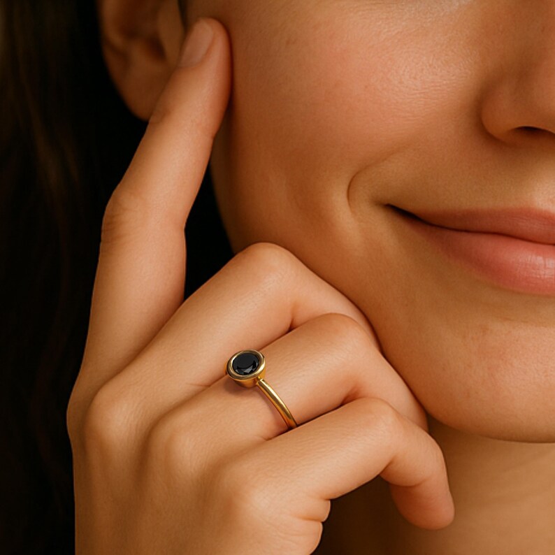 A close-up of a person's hand wearing a gold ring with a blue gemstone, resting on the person's chin.