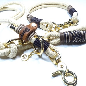 May include: A white rope dog leash and collar set with brown and black accents. The leash has a gold metal clasp and a leather tag with the word "Brown" engraved on it. The collar has a gold metal buckle.