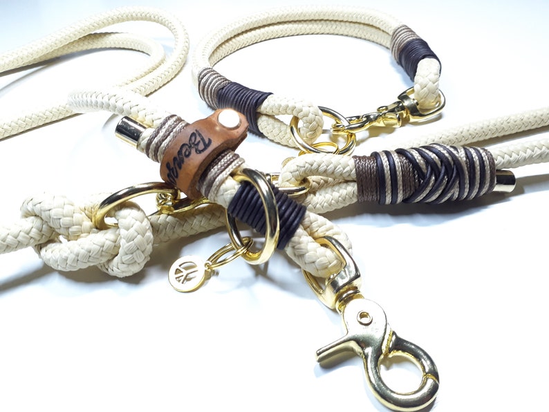 May include: A white rope dog leash and collar set with brown and black accents. The leash has a gold metal clasp and a leather tag with the word "Brown" engraved on it. The collar has a gold metal buckle.