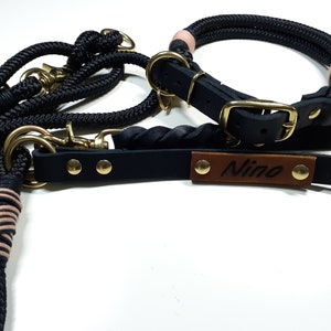 May include: Black leather dog collar and leash set with a brown leather tag that says "Nino". The collar is made of rope and has pink accents.