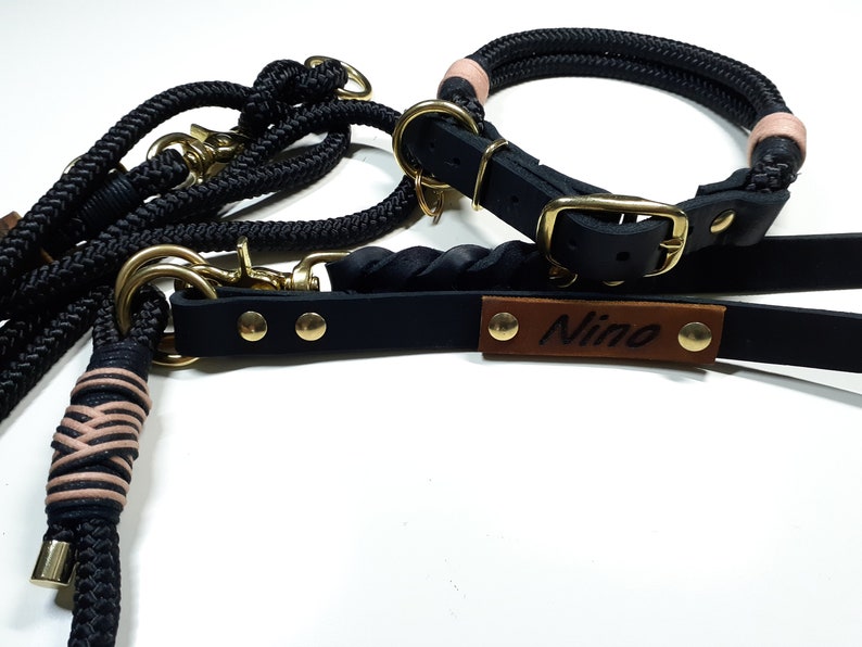 May include: Black leather dog collar and leash set with a brown leather tag that says "Nino". The collar is made of rope and has pink accents.