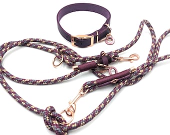 May include: A purple leather dog collar with a gold buckle and matching leash set. The leash is made of a rope-like material with a mix of purple, gray, and cream colors. The set includes a collar, a leash, and a matching charm.