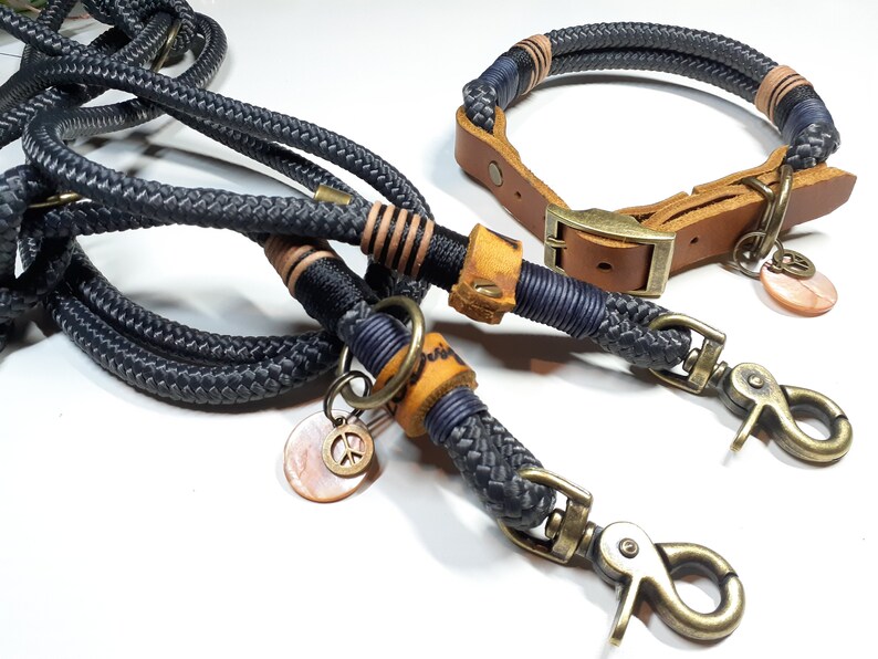 以下が含まれることがあります： 黒とネイビーのロープ製の犬用リードとカラーのセット。茶色の革のアクセントと平和のシンボルのチャームが付いています。