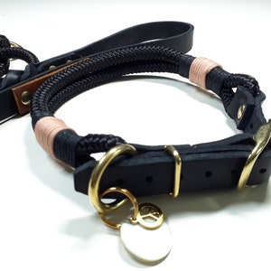 May include: Black leather dog collar with a rope leash and a gold peace sign charm. The collar has a buckle closure and the leash is made of black rope with a pink accent.