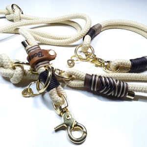 May include: A white rope dog leash and collar set with brown accents. The leash has a gold metal clasp and a leather tag that says "Bear".