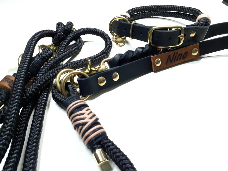 May include: Black rope dog leash with a pink and black braided accent and a gold metal clasp. A black leather dog collar with gold hardware and a brown leather tag that says "Nino".