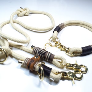 May include: A white rope dog leash and collar set with brown leather accents and gold metal hardware. The leash has a loop at one end and a clip at the other. The collar has a clip and a D-ring. The leather accents have the word "Bear" embossed on them.