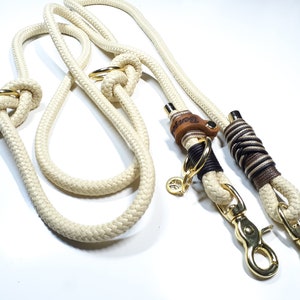 May include: A white rope dog leash with two gold metal clips and a brown leather tag with the word "Rover" engraved on it.