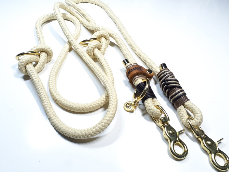 May include: A white rope dog leash with two gold metal clips and a brown leather tag with the word "Rover" engraved on it.