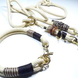 May include: A white rope dog collar and leash set with brown and beige accents. The leash has a gold metal clasp and a leather tag with the word "Bespoke" embossed on it.