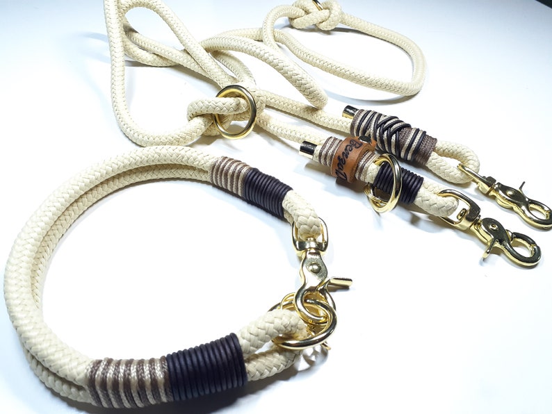 May include: A white rope dog collar and leash set with brown and beige accents. The leash has a gold metal clasp and a leather tag with the word "Bespoke" embossed on it.