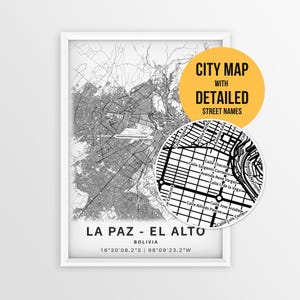 Op de afbeelding: Een ingelijste zwart-wit kaart van La Paz en El Alto, Bolivia, met gedetailleerde stratenplannen en coördinaten. Een cirkelvormige uitsnede toont specifieke straatnamen, met een geel label met de tekst CITY MAP WITH DETAILED STREET NAMES.