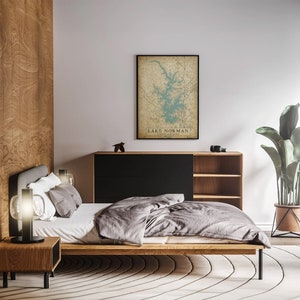 Puede incluir: Un dormitorio moderno con una cama de madera, una colcha gris y una mesita de noche con una l&aacute;mpara. Un mapa enmarcado del lago Norman, Carolina del Norte, cuelga de la pared. La habitaci&oacute;n tiene un dise&ntilde;o moderno con colores neutros y una gran planta en maceta.