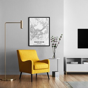 May include: A framed black and white map print of Madison, Wisconsin, featuring detailed street grids and water bodies. The text reads MADISON, WISCONSIN, and the coordinates 43&deg;04'25.0"N 89&deg;23'08.0"W are printed clearly at the bottom of the poster.