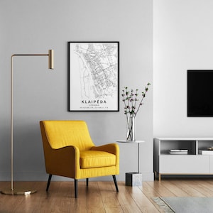 May include: A modern living room scene featuring a yellow armchair with black legs, a framed map of Klaipėda, Lithuania, and a gold floor lamp. A side table holds a vase of flowers. The room has a minimalist design.