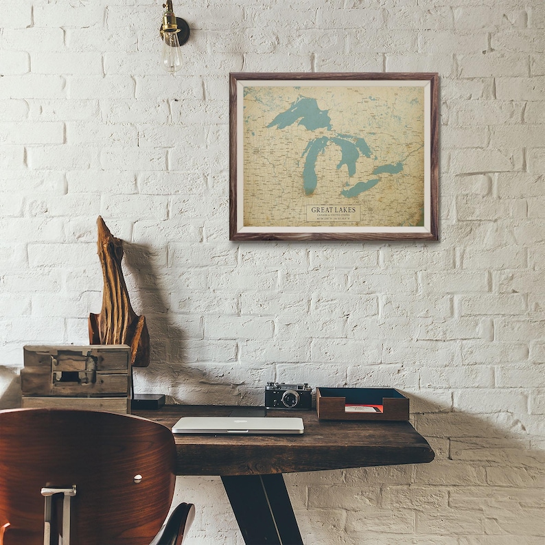 Puede incluir: Un mapa enmarcado de los Grandes Lagos, con los lagos en color azul claro, cuelga de una pared de ladrillos blancos. El mapa est&aacute; en un marco de madera marr&oacute;n. El texto "GREAT LAKES" es visible en el mapa. Un escritorio con una computadora port&aacute;til, una c&aacute;mara y otros elementos est&aacute; en primer plano.