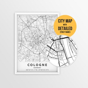 May include: A black and white city map print of Cologne, Germany, in a white frame. The map includes detailed street names and coordinates. A circular inset highlights a section of the map.