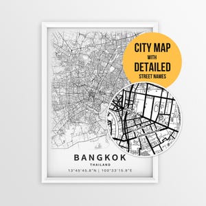 May include: A framed black and white map of Bangkok, Thailand, featuring a detailed street grid, coordinates, and a circular inset showing street names like Rama IV Rd and Si Lom Rd. A yellow circular graphic reads CITY MAP WITH DETAILED STREET NAMES.