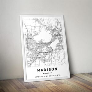 May include: A framed vertical wall art print featuring a black and white street map of Madison, Wisconsin. The print includes the text MADISON, WISCONSIN, and the coordinates 43&deg;04'25.8"N | 89&deg;23'28.9"W printed in a clean, sans-serif font at the bottom.