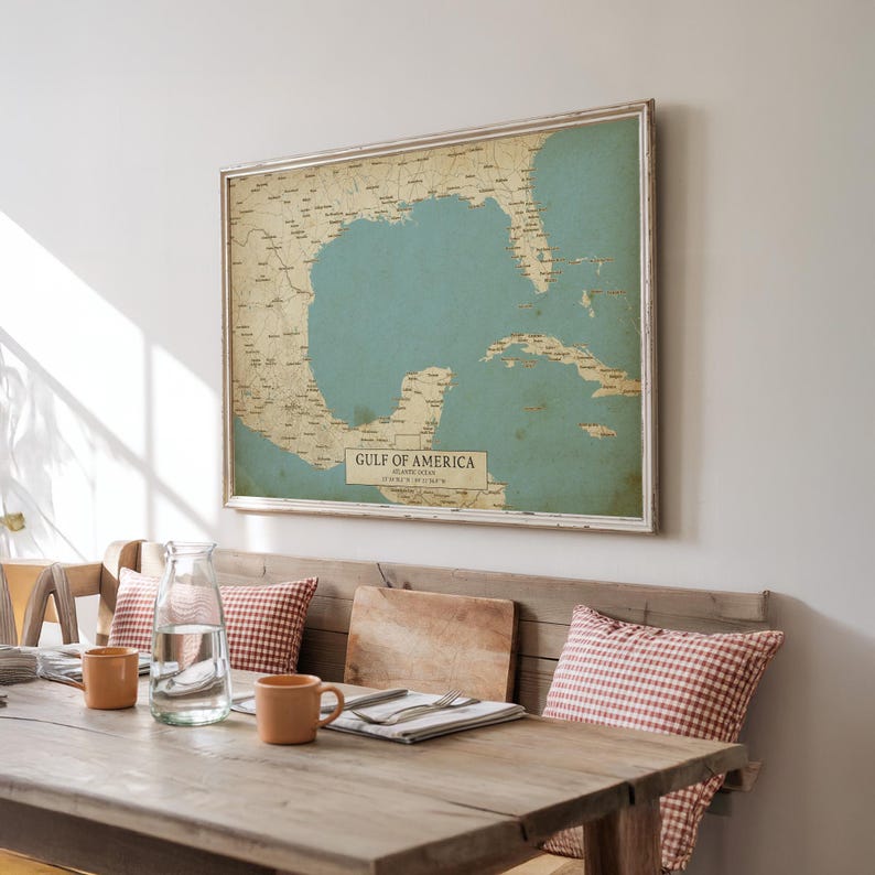 Puede incluir: Un mapa enmarcado del Golfo de Am&eacute;rica, con un mar azul claro y masas terrestres beige. El mapa est&aacute; en un marco blanco y cuelga sobre un banco de madera con cojines a cuadros rojos y blancos. El texto "GULF OF AMERICA" es visible.