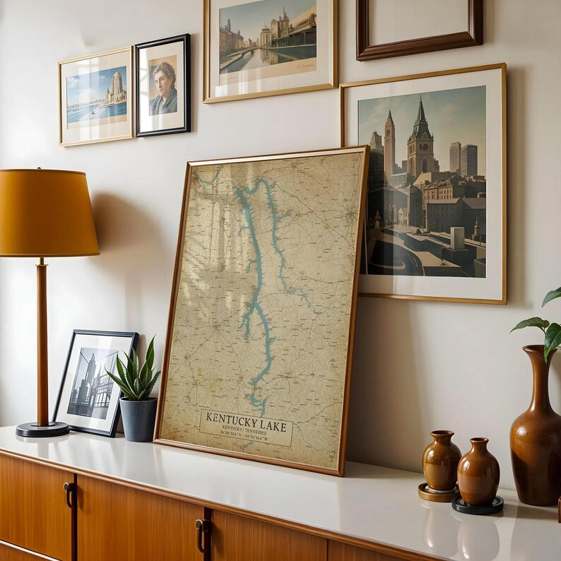 Puede incluir: Un mapa enmarcado de estilo vintage del lago Kentucky, con detalles azules para el agua y beige para la tierra. El mapa se exhibe sobre una superficie blanca, junto a grabados art&iacute;sticos enmarcados y una l&aacute;mpara moderna. El texto "Kentucky Lake" es visible.