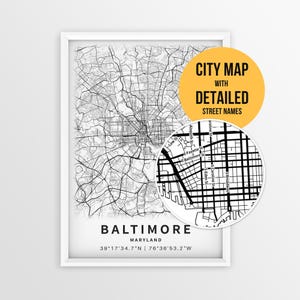 May include: A framed black and white map print of Baltimore, Maryland, featuring a grid of streets and coordinates. A circular inset shows a magnified view of street names like E Fayette St and S Broadway. Text reads CITY MAP WITH DETAILED STREET NAMES.