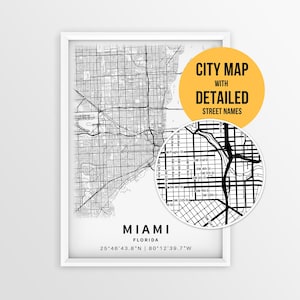 May include: A framed black and white map of Miami, Florida, featuring a grid of streets and coordinates. A circular inset shows a magnified view of the street layout with labels like W Flagler St and SW 2nd St. A yellow circle contains the text CITY MAP WITH DETAILED STREET NAMES.