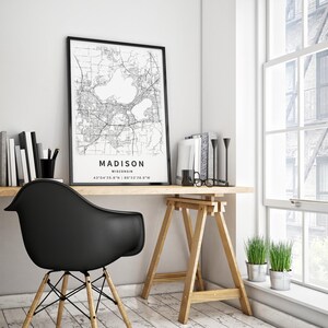 May include: A black and white map print of Madison, Wisconsin, framed in a thin black frame. The map displays city streets and two prominent lakes, with the text MADISON, WISCONSIN, and the coordinates 43&deg;04'25.8"N 89&deg;23'28.9"W printed below.